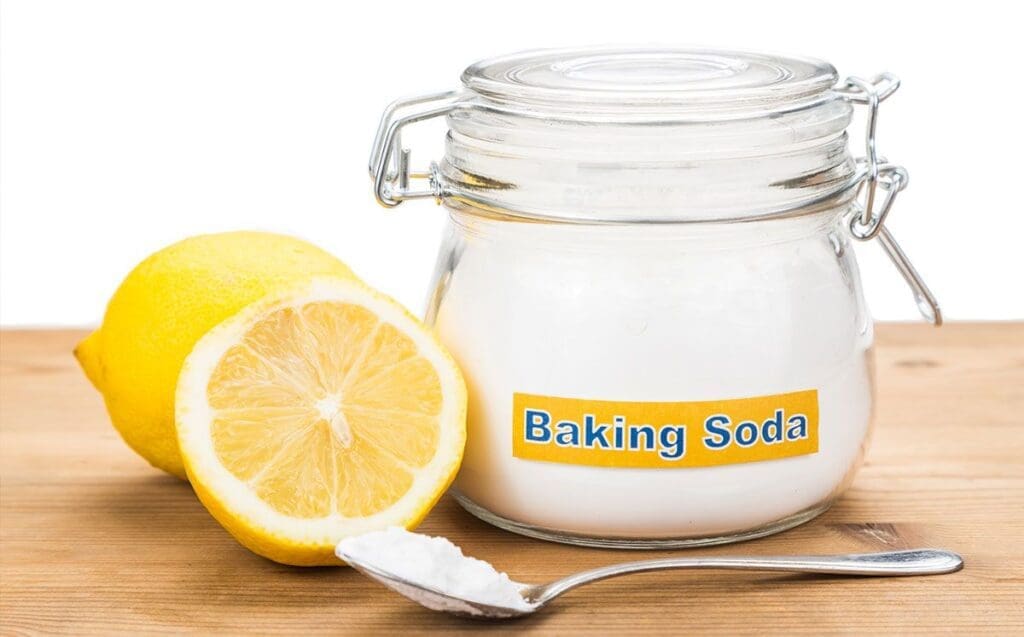 baking soda jar and lemon with a spoon filled with baking soda on a table surface