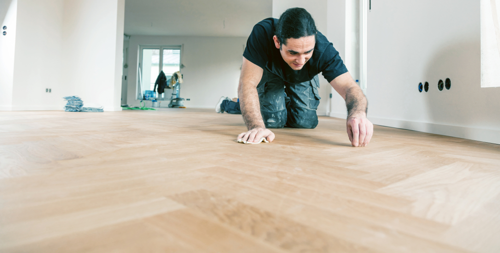 paint spilled on vinyl floor and a person is removing it on his knees.