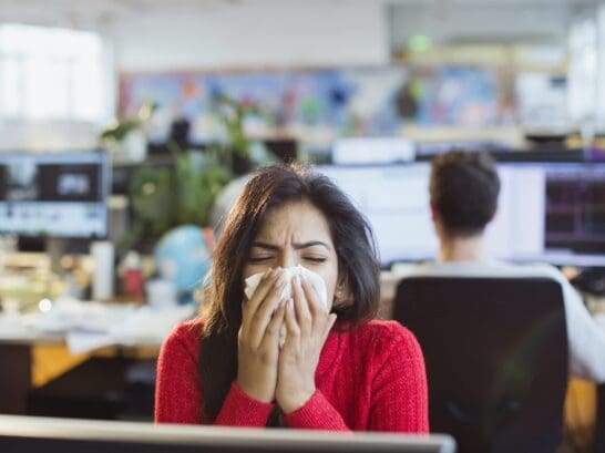 A woman works at her desk though she is sick